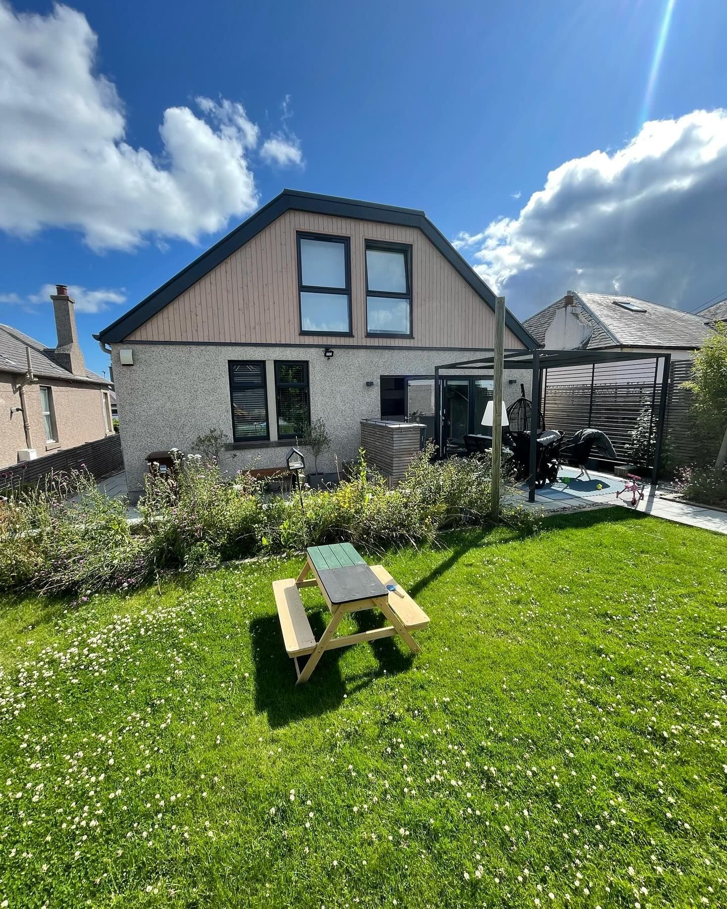 The finished bungalow with a new timber-clad gable and two upper windows, seen across a sunny lawn.