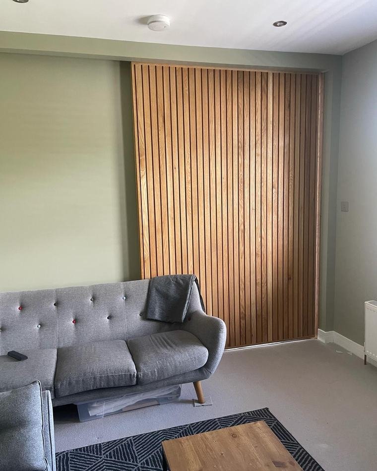 A floor-to-ceiling sliding door in vertical oak slats in a living room.