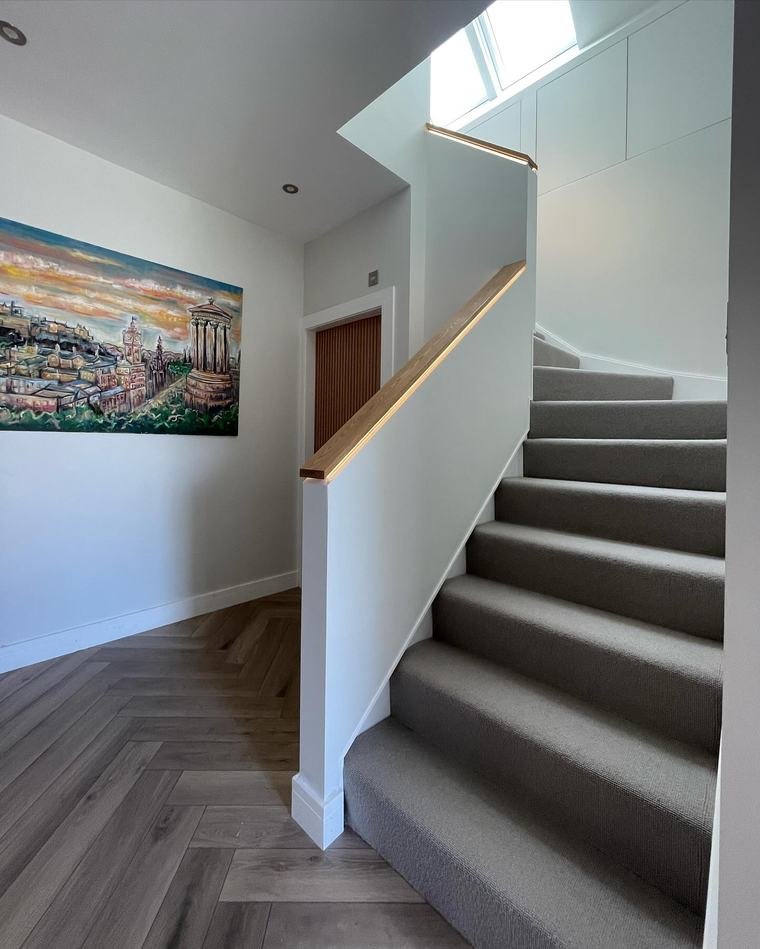 New staircase with an oak handrail lit by an LED channel, above herringbone flooring.