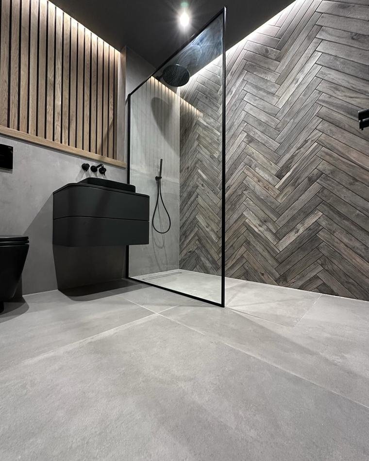 En-suite with slatted oak panelling, a black wall-hung basin, large grey floor tiles and a herringbone timber wall in the shower.