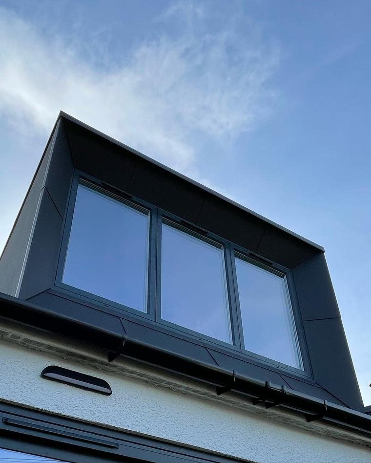 A black zinc-clad dormer with three windows on a white-rendered Edinburgh house, seen from below against a blue sky.