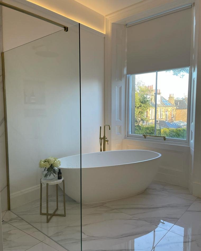 Marble-tiled bathroom with a freestanding bath beneath a sash window that looks out over Edinburgh rooftops.