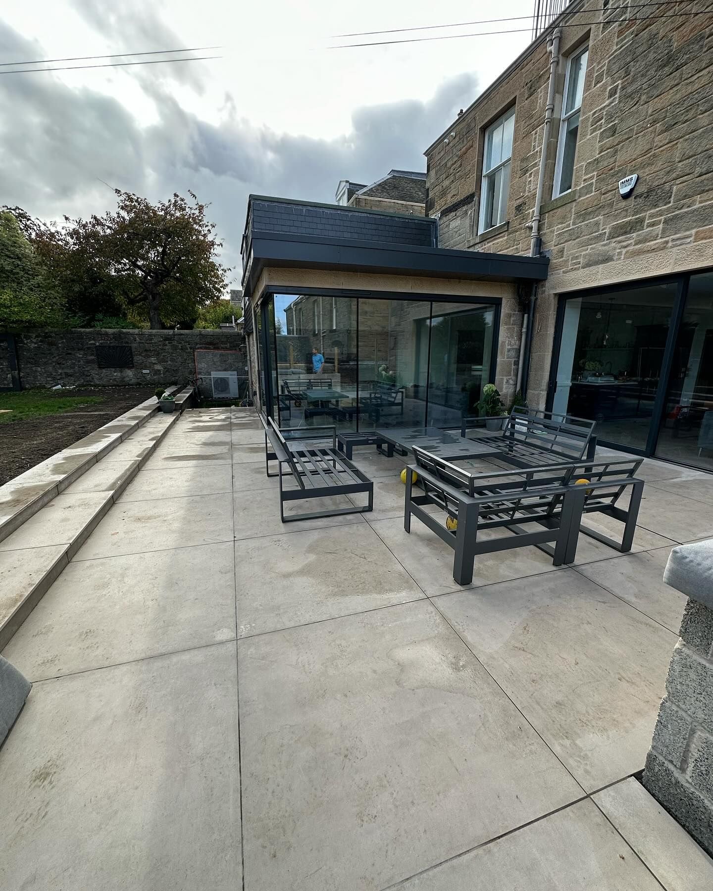 The rear of a sandstone villa in Morningside with a new frameless glass corner extension opening onto a large stone patio.